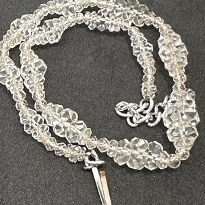 May include: A silver chain necklace featuring a clear crystal bead design. The necklace is made from small, faceted crystals strung together in a repeating pattern. The necklace has a simple clasp closure.