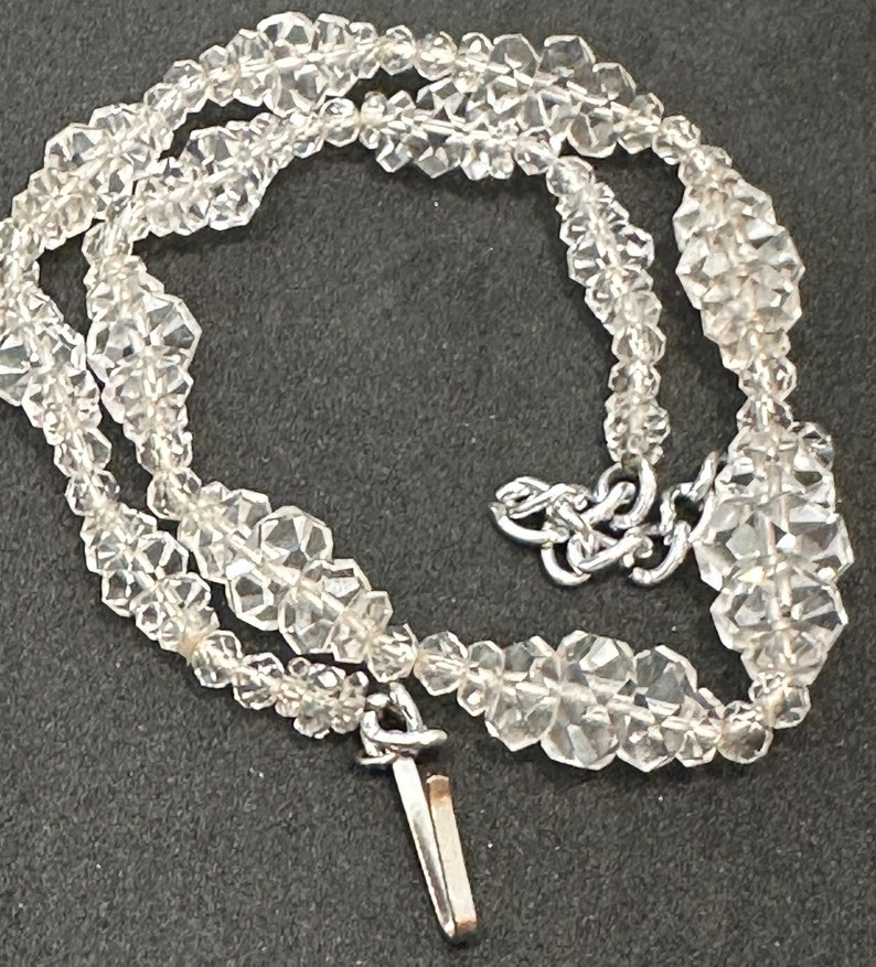May include: A silver chain necklace featuring a clear crystal bead design. The necklace is made from small, faceted crystals strung together in a repeating pattern. The necklace has a simple clasp closure.