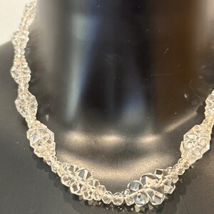 May include: A clear crystal necklace featuring faceted beads. The necklace is crafted from numerous small, faceted crystals strung together to create a delicate and elegant design.