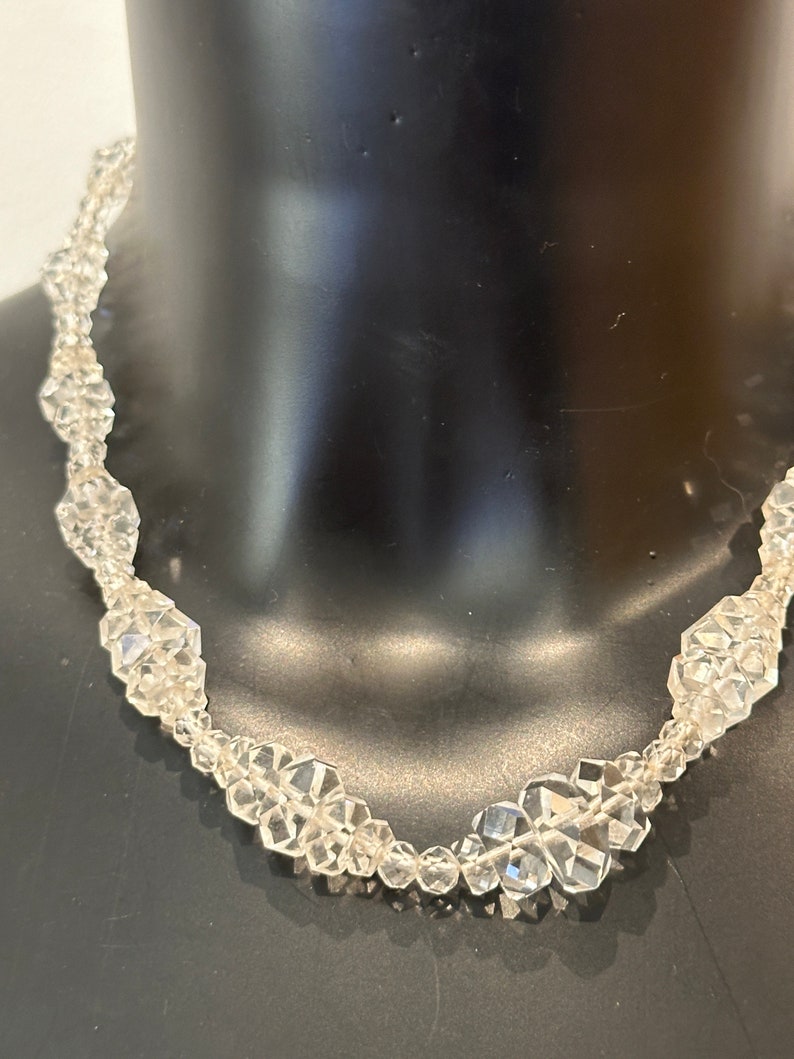 May include: A clear crystal necklace featuring faceted beads. The necklace is crafted from numerous small, faceted crystals strung together to create a delicate and elegant design.