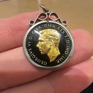 May include: A silver pendant with a black and gold coin featuring a profile of King George VI. The coin has the inscription "GEORGIVS VI D.G.BR.OMN.REX F.D.IND.IMP."