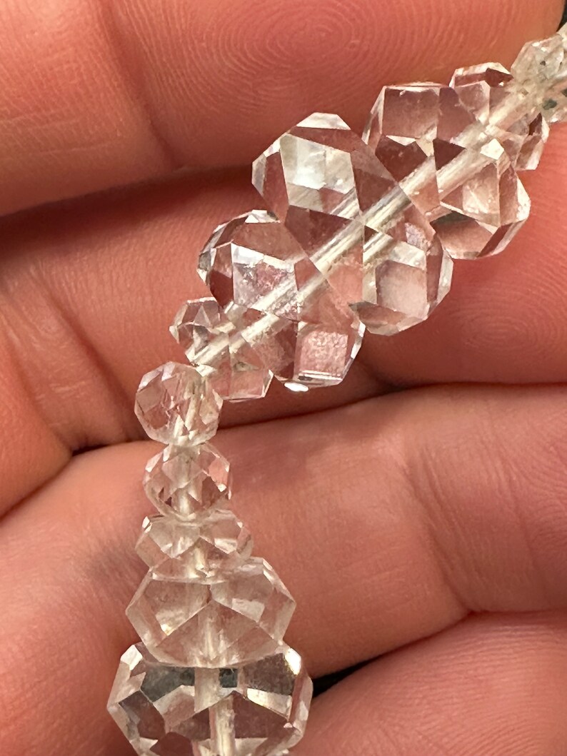 May include: A strand of clear quartz crystal beads, each bead is faceted and has a unique shape. The beads are strung on a silver wire.