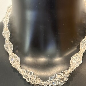 May include: A clear crystal necklace with faceted beads. The necklace is on a black mannequin.