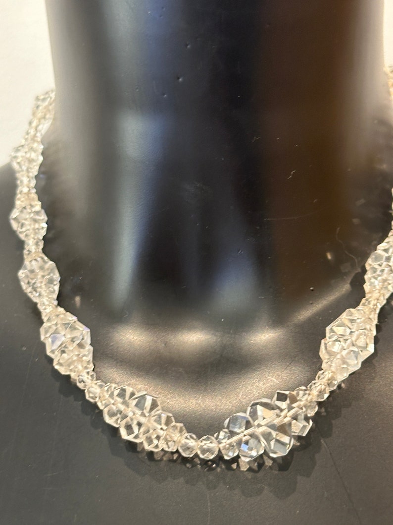 May include: A clear crystal necklace with faceted beads. The necklace is on a black mannequin.