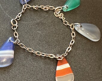 Pode incluir: Um bracelete de corrente de prata com cinco pedras de ágata em forma de lágrima. As pedras são em tons de azul, verde e laranja.