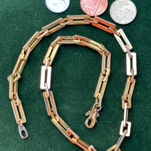 Puede incluir: Un collar de cadena de oro con un diseño de eslabones cuadrados. La cadena está hecha de dos tonos de oro diferentes, con un cierre en el extremo.
