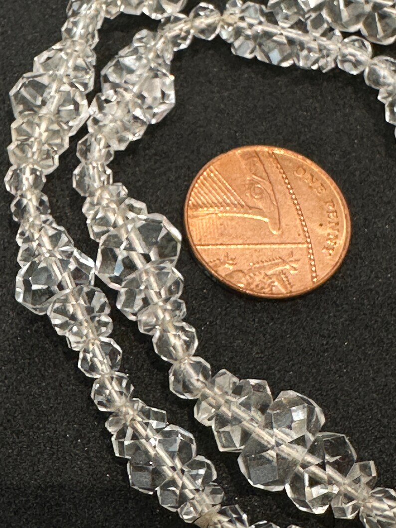 May include: A strand of clear faceted crystal beads, shown next to a British one penny coin for scale.