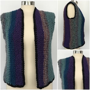 May include: A sleeveless knitted vest with a striped pattern in shades of teal, purple, and brown. The vest has a black trim around the neckline and armholes.