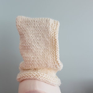 Könnte beinhalten: Ein weißer gestrickter Schal mit einem umgeklappten Saum. Der Schal ist aus weichem, dickem Garn gefertigt.