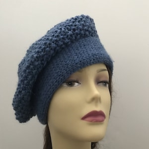May include: A blue knitted beret with a textured pattern. The beret is worn on a mannequin head.