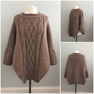 May include: A brown cable knit sweater with a loose fit and a wide neckline. The sweater has a cable knit pattern on the front and back.