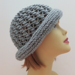 May include: A gray crocheted hat with a wide brim and a lacy pattern. The hat is worn by a mannequin with short, reddish-brown hair.