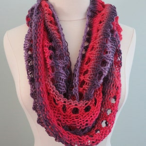 May include: A crocheted infinity scarf in shades of pink and purple. The scarf is made with a lacy stitch pattern and has a soft, drapey feel.
