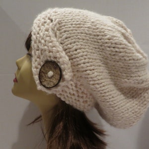 May include: A cream-colored knitted beanie with a large brown button on the side.