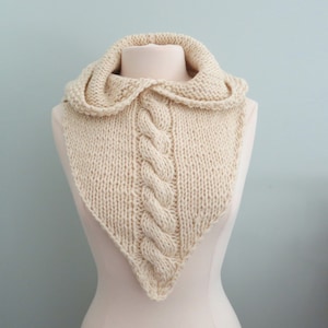 May include: A cream-coloured knitted cowl with a cable knit pattern and a hood.