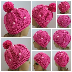 Puede incluir: Sombrero de punto rosa con un pompón blanco y adornos de perlas. El sombrero tiene un diseño floral.