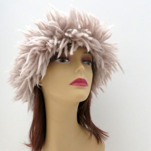 May include: A fluffy, light beige headband made of yarn. The headband is worn on a mannequin with brown hair.