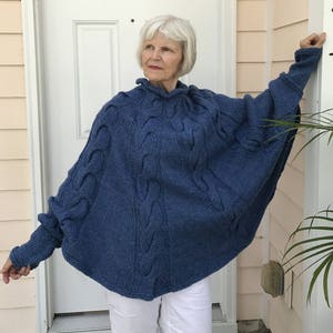 May include: A blue knitted poncho with a cable knit pattern. The poncho has a high neck and long sleeves.