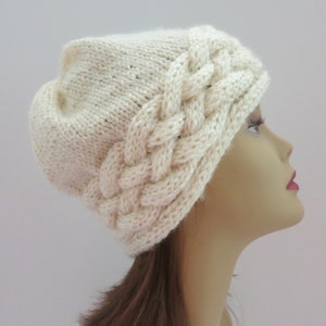 May include: A white knitted hat with a braided design around the brim.