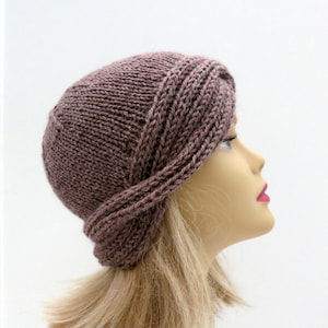 Può includere: Un cappello di lana marrone con un design piegato. Il cappello è realizzato con un filato morbido e testurizzato.