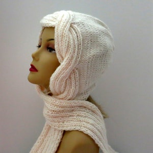 May include: A white knitted hat and scarf set with a cable knit design. The hat has a long, flowing design that covers the ears and neck.