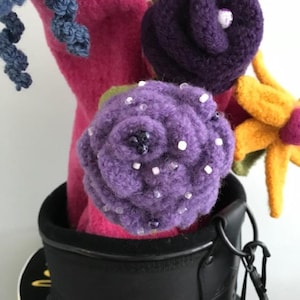 May include: A close-up of a purple felt flower with white beads, in a black felt flower pot. The flower is part of a bouquet of felt flowers.