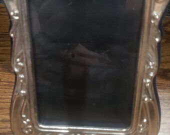 May include: A silver picture frame with an ornate design. The frame has a raised edge and a smooth, reflective surface.