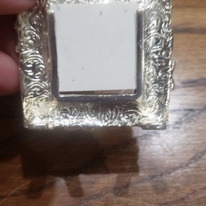 May include: A silver-toned picture frame with an ornate design. The frame has a white background and is empty.