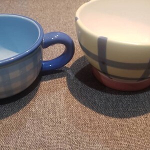 May include: Two ceramic mugs with blue and white checkered patterns. One mug is blue with a white check pattern, the other is yellow with a blue check pattern.