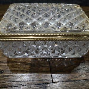 May include: A clear glass box with a gold trim around the lid. The box has a diamond pattern on the top and bottom.