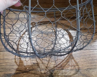 May include: A gray metal wire basket with a rounded shape. The basket is made of a wire mesh and has a handle on the top.