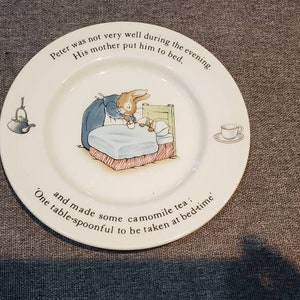 May include: White ceramic plate with a blue and white illustration of Peter Rabbit in bed. The plate has text that reads "Peter was not very well during the evening. His mother put him to bed. and made some camomile tea. One table-spoonful to be taken at bedtime."