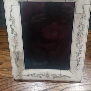 May include: A white picture frame with a black mat and a floral design. The frame is made of bone and has a delicate, intricate design.