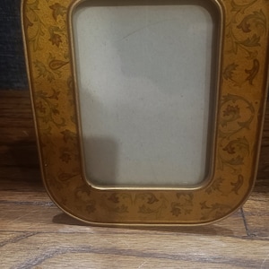 May include: A gold picture frame with a floral design. The frame has a rounded top and bottom and a rectangular opening for a photo.