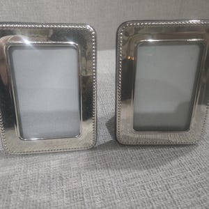 May include: Two silver rectangular picture frames with a beaded border. The frames have a shiny finish and a simple, elegant design. The frames are empty, ready to display photos.