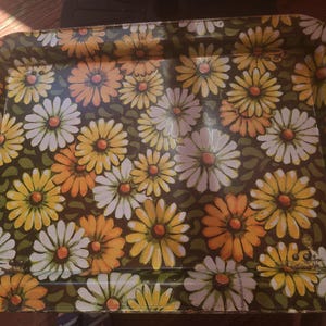 May include: A rectangular metal serving tray featuring a repeating floral pattern of daisies in shades of white, yellow, and orange set against a dark brown background with green leaf accents. The tray has raised edges and a glossy finish.