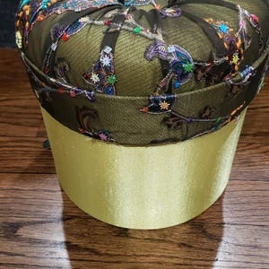May include: A green and black fabric ottoman with a floral pattern. The ottoman has a round top and a cylindrical base.