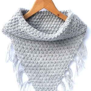 Könnte beinhalten: Ein grauer gestrickter Schal mit Schalkragen und Fransen. Der Schal ist mit einem strukturierten Stich gearbeitet und hat ein schlichtes, modernes Design.