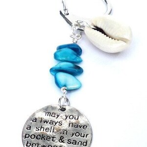 Könnte beinhalten: Ein silberner Schlüsselanhänger mit einem blauen und weißen Muschel-Anhänger und einem silbernen Anhänger mit dem Text "may you always have a shell in your pocket & sand between your toes".