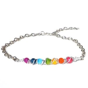 May include: A silver chain bracelet with seven colourful beads in a rainbow pattern.
