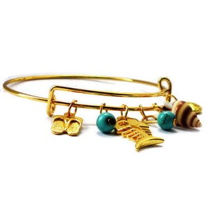 Peut inclure: Un bracelet jonc en or avec des breloques, dont un coquillage, un poisson et des tongs. Les breloques sont attachées au bracelet avec de petits anneaux en or.
