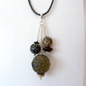 Puede incluir: Un collar de cadena de plata con un colgante de cuentas de vidrio con estampado verde, marrón y negro. El colgante tiene una tapa de plata en la parte inferior.