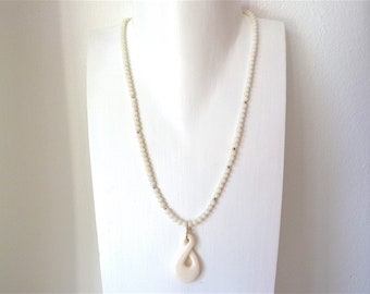 Puede incluir: Collar de perlas blancas con un colgante de hueso blanco en forma de nudo.