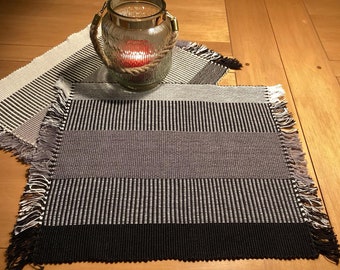 Set of 2 rectangular placemats, the first black and white, the second white and black. Hand-woven, rectangular in shape.