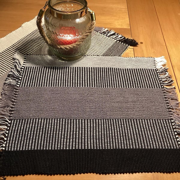 Set of 2 rectangular placemats, the first black and white, the second white and black. Hand-woven, rectangular in shape.