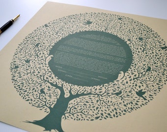 May include: A square piece of tan paper featuring a circular dark green tree illustration with birds nestled in the branches. The center contains printed text and blank lines for signatures labeled Bride, Groom, Rabbi, and Witness. A black fountain pen lies nearby.