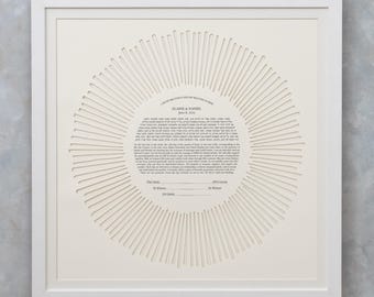 May include: A framed, off-white paper artwork with a circular design. The artwork features a central text surrounded by radial lines, all within a white frame. The text includes names and a date.