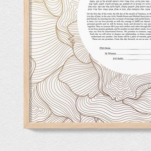 May include: A framed Ketubah, a Jewish marriage contract, with elegant gold-colored line art and text. The document includes the words "Bride", "Witness", and "Rabbi". The design features a light wood frame.