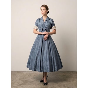 May include: A slate blue midi-length dress featuring a V-neckline, short sleeves with cream-colored lace cuffs, and a fitted bodice with a central bow detail. The skirt is full and pleated, falling below the knees in a structured, shimmering fabric.