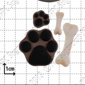May include: Silicone mold for baking dog paw prints and bones. The mold is white and shows a large paw print, a small paw print, and two bones. There are also three smaller paw prints in the mold. The mold is 1 cm in size.